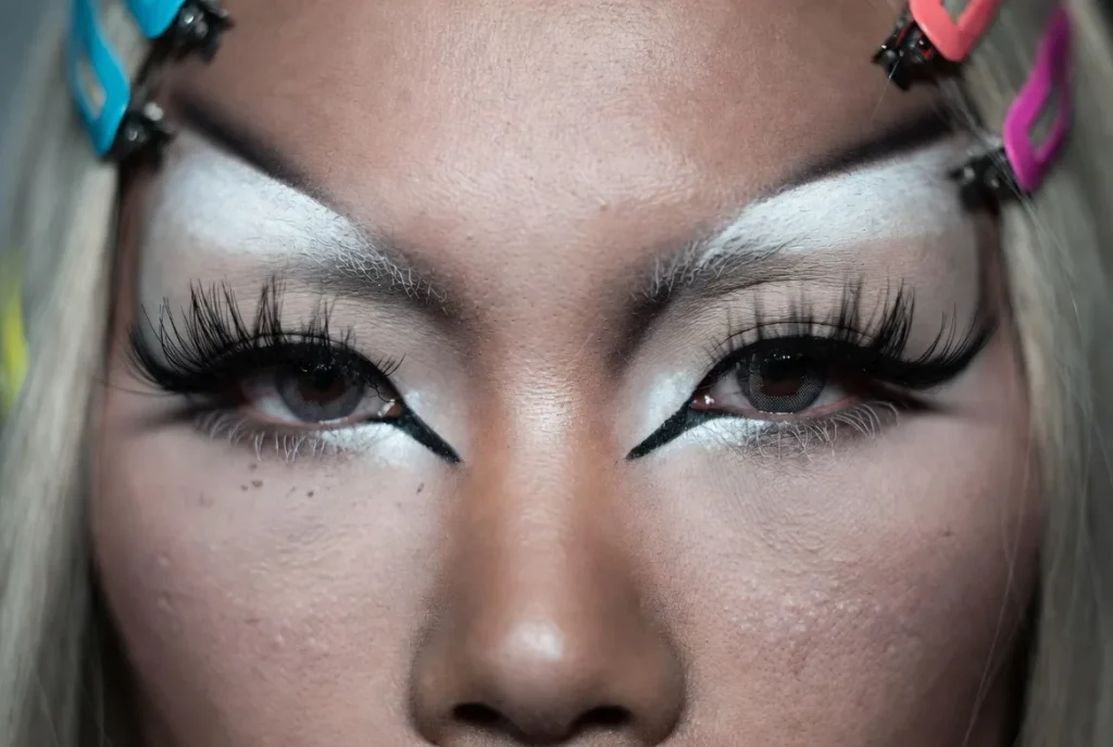 Close extremo de maquiagem yamanba com grandes detalhes brancos no rosto, delineador preto e cílios longos em cabelo loiro platinado, textura de pele realista e pequenas imperfeições