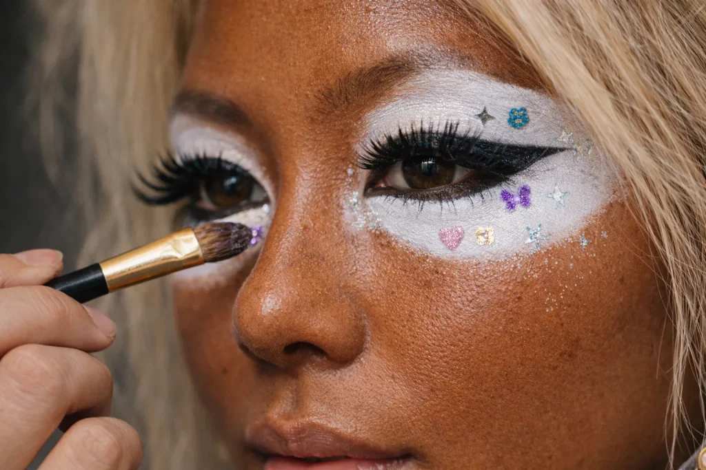 Extreme close-up of yamanba makeup application on deep tanned skin, large white accents, black liner and long lashes, realistic skin pores and makeup brush, authentic gyaru beauty photo