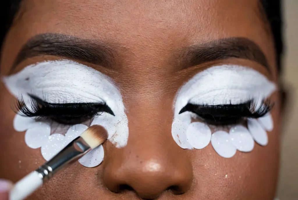 深い日焼けの肌、大きな白いアクセント、黒いライナー、長いまつげ、リアルな肌の毛穴とメイクブラシ、本格的なギャルビューティーの写真のヤマンバメイクアップの極端なクローズアップ。