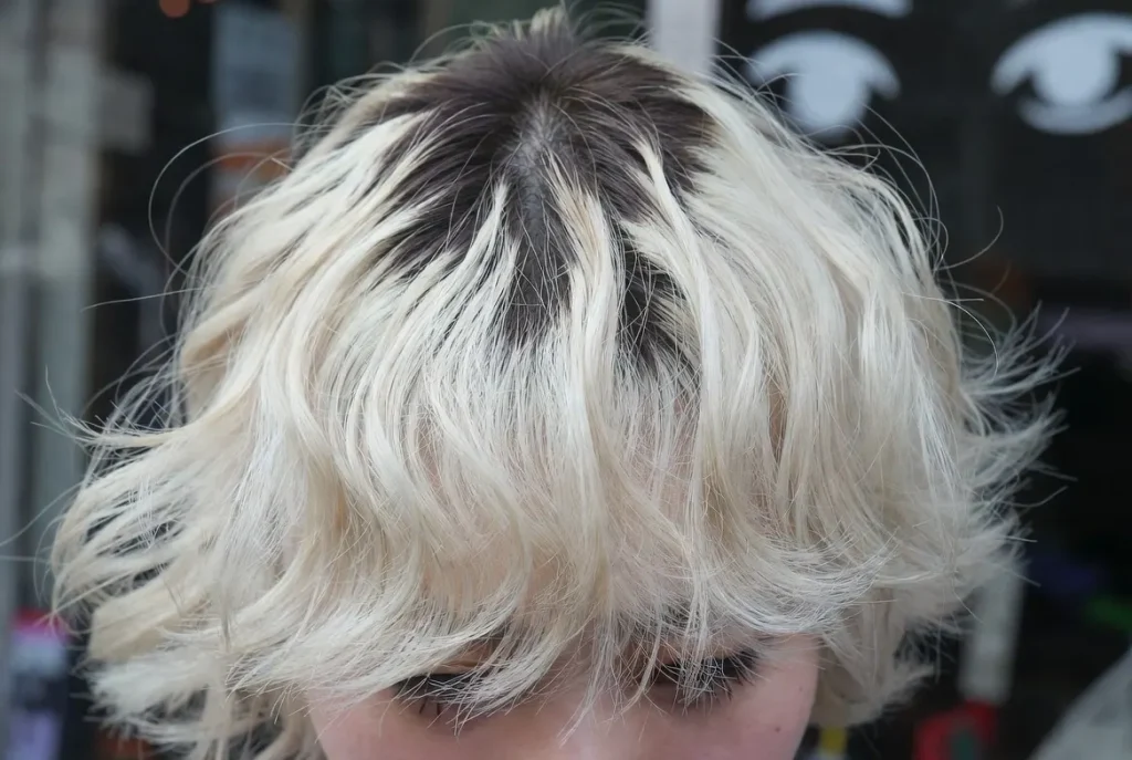 Gros plan sur les cheveux blonds platine décolorés de Ganguro gyaru, avec des racines foncées et un volume massif, un contraste dramatique.