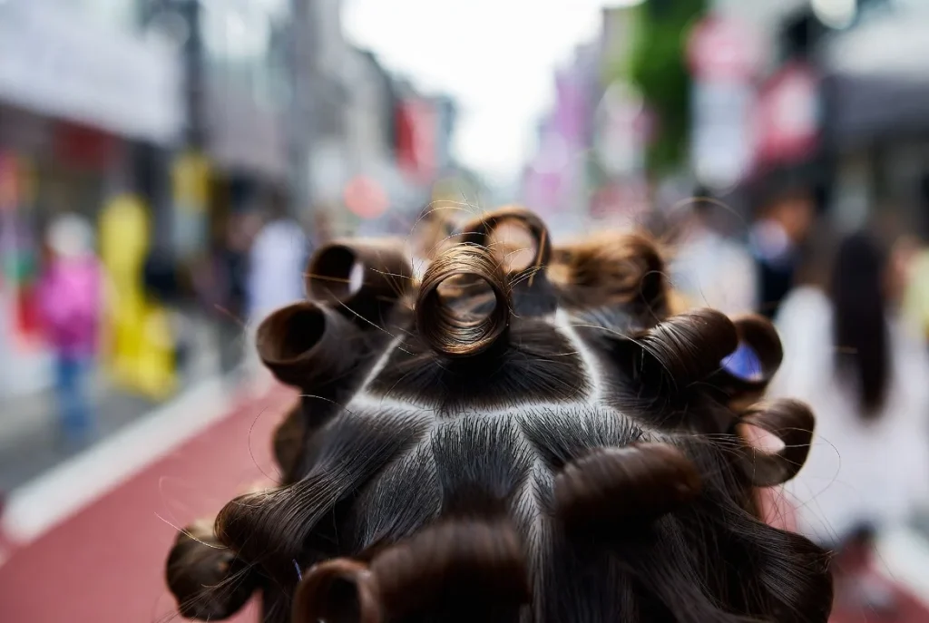 Gros plan sur la technique de coiffure gyaru de Sujimori montrant de minuscules sections carrées peignées et bouclées, texture détaillée des cheveux.