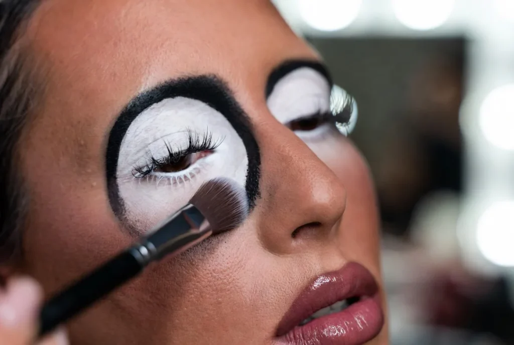 ganguro makeup close up white eye shadow circles dramatic black eyeliner long lashes deep tanned skin makeup brush applying product